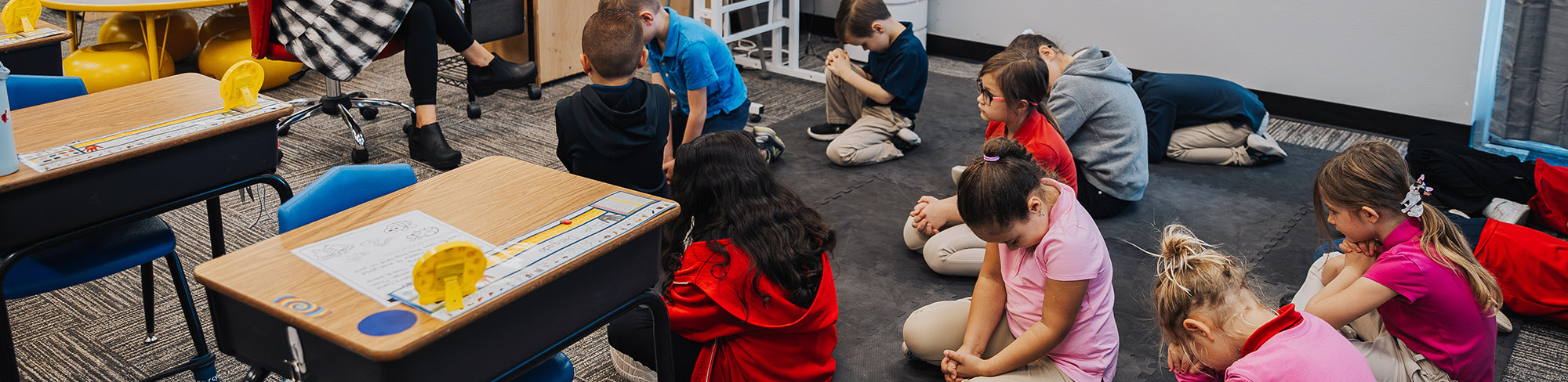 Elementary students praying and sitting on the classroom floor